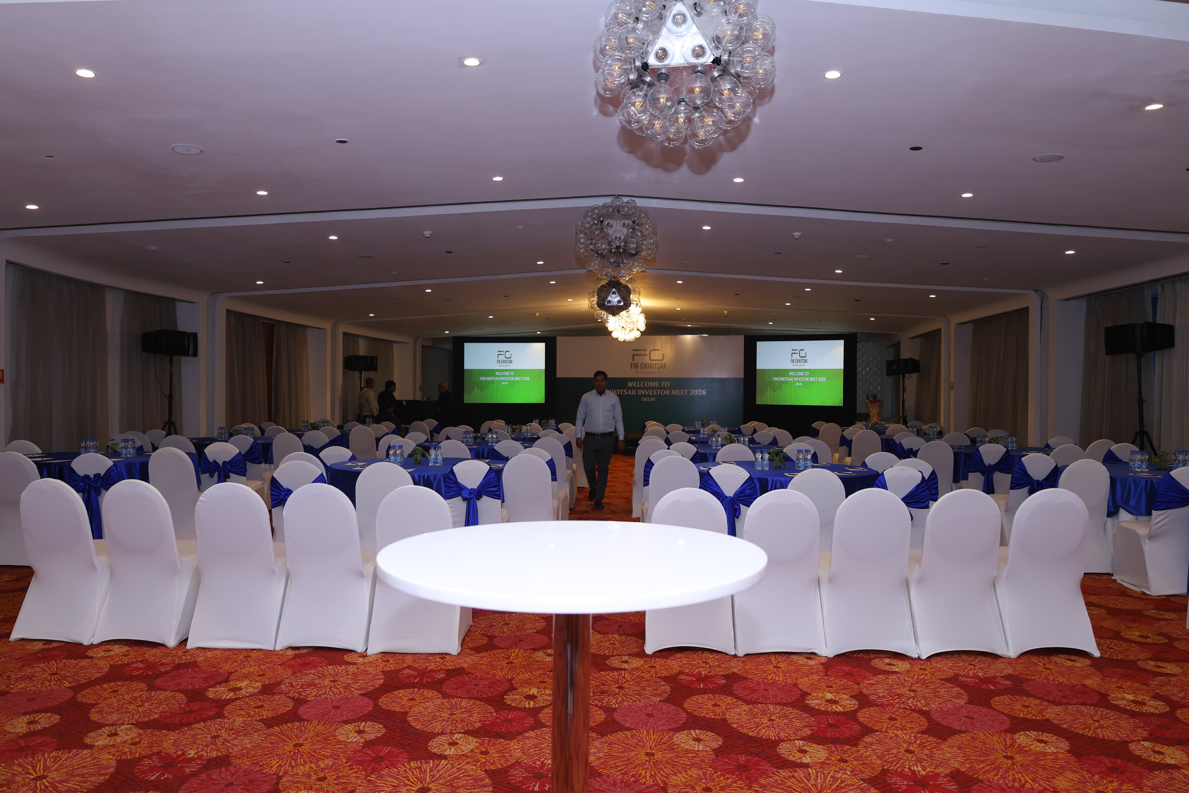 Large conference hall with round tables, stage, and investor meet branding
